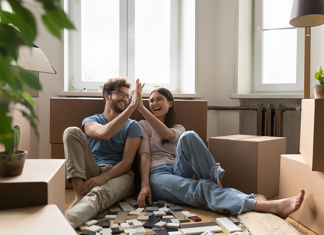 Insurance Solutions - Portrait of a Cheerful Young Couple Giving Each Other High Five as They Sit Next to Moving Boxes in Their New Apartment