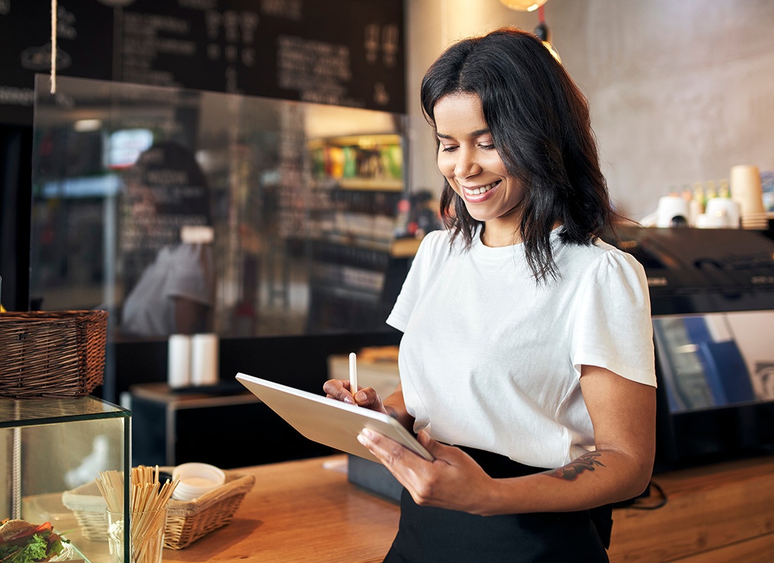 Service Center - Closeup Portrait of a Cheerful Young Female Business Owner Using a Tablet as she Stands Inside her Cafe by the Front Counter